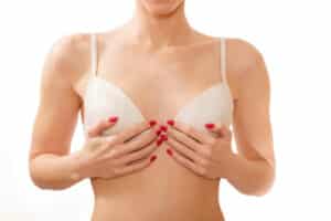 Woman in white bra covering her small breast with her hands