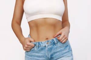 Woman in jeans showing off her toned, flat midsection after tummy tuck in Savannah, GA